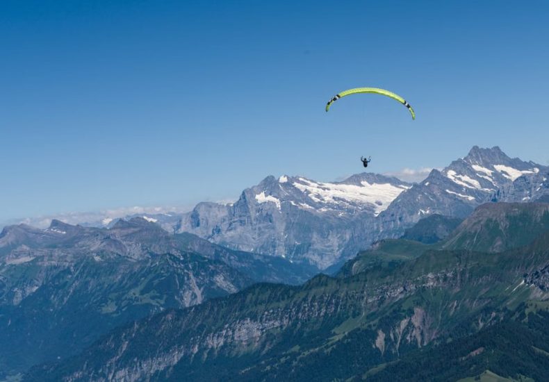 A paraglider soaring above the picturesque Swiss Alps with clear blue skies and stunning mountain views.